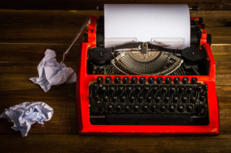 Typewriter with crumpled sheets. On wooden background.