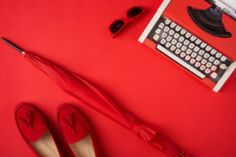 Bright red shoes, umbrella , typewriter and glasses lying on red background